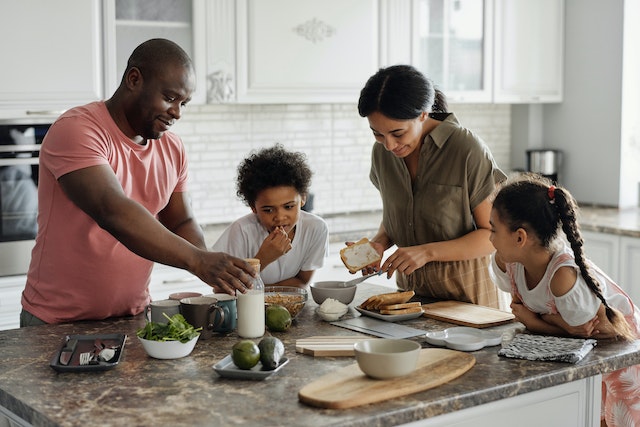 Two parents and their children prepare breakfast on a kitchen island with a granite countertop in a newly upgraded rental